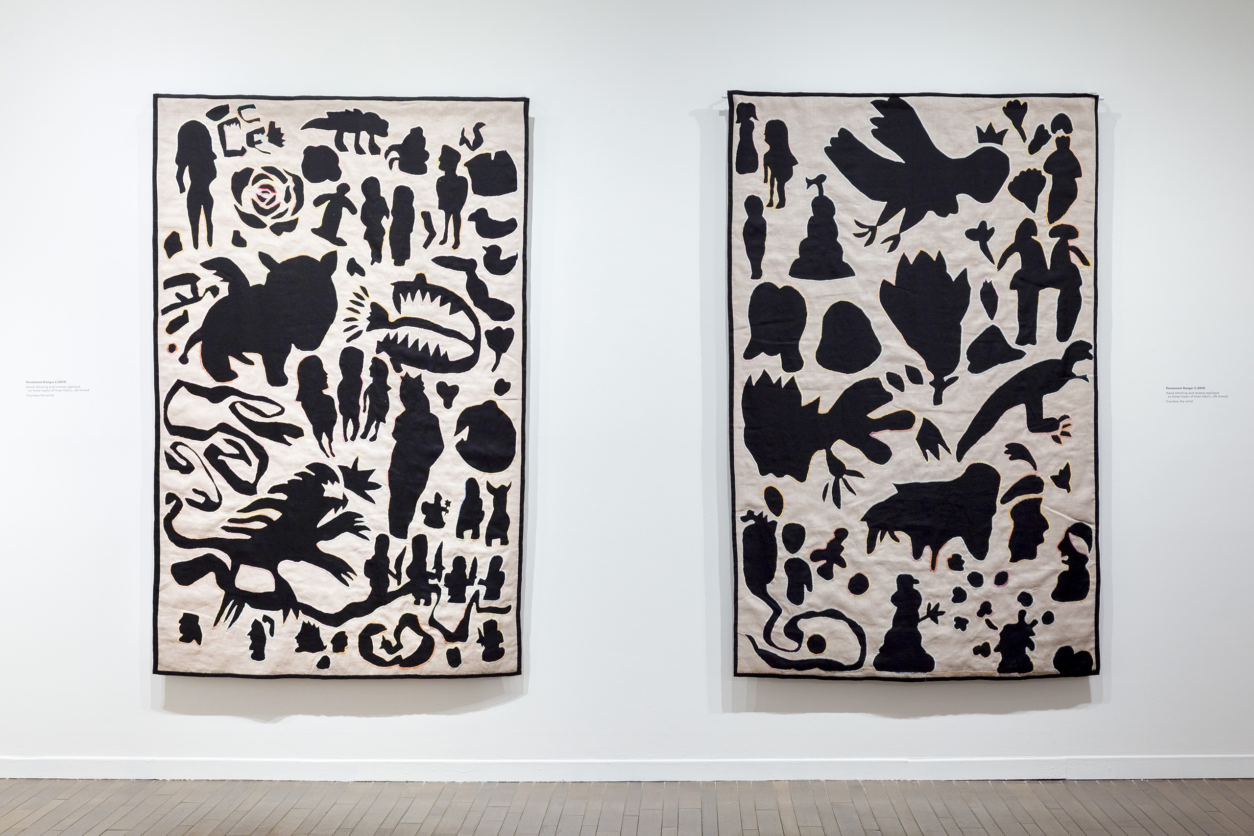 Two large embroidered hangings with black shapes and silhouettes of fantasy creatures on a tan ground colour.