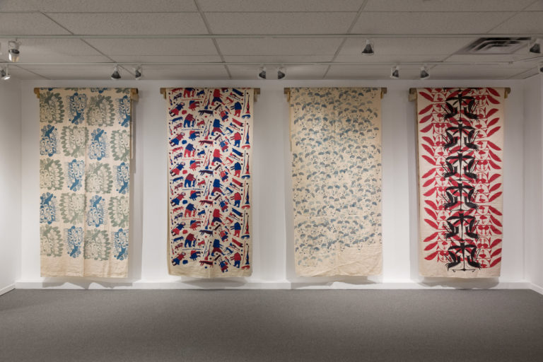 Image shows 4 pieces of printed textiles in an exhibition