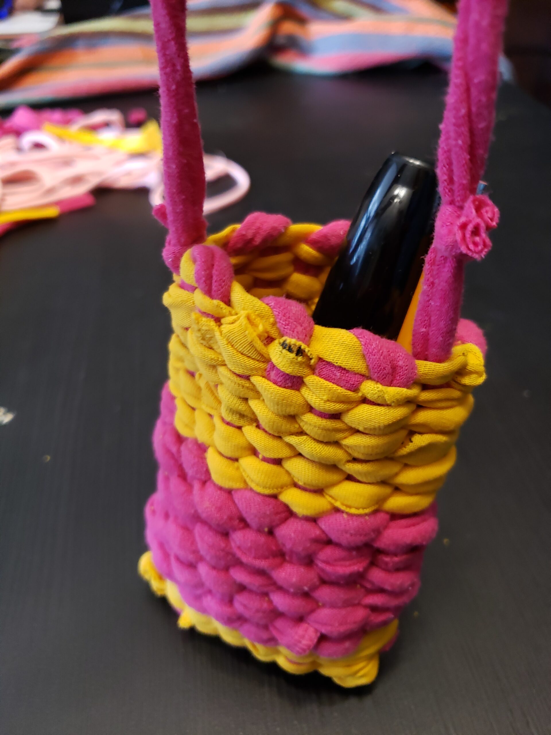 A yellow and pink pouch, woven with yarn created from t-shirt holds a pen.