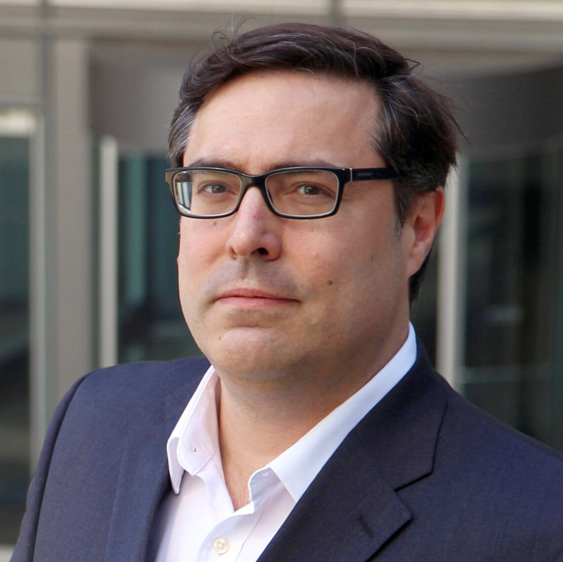 Man with dark hair and glasses in a suit