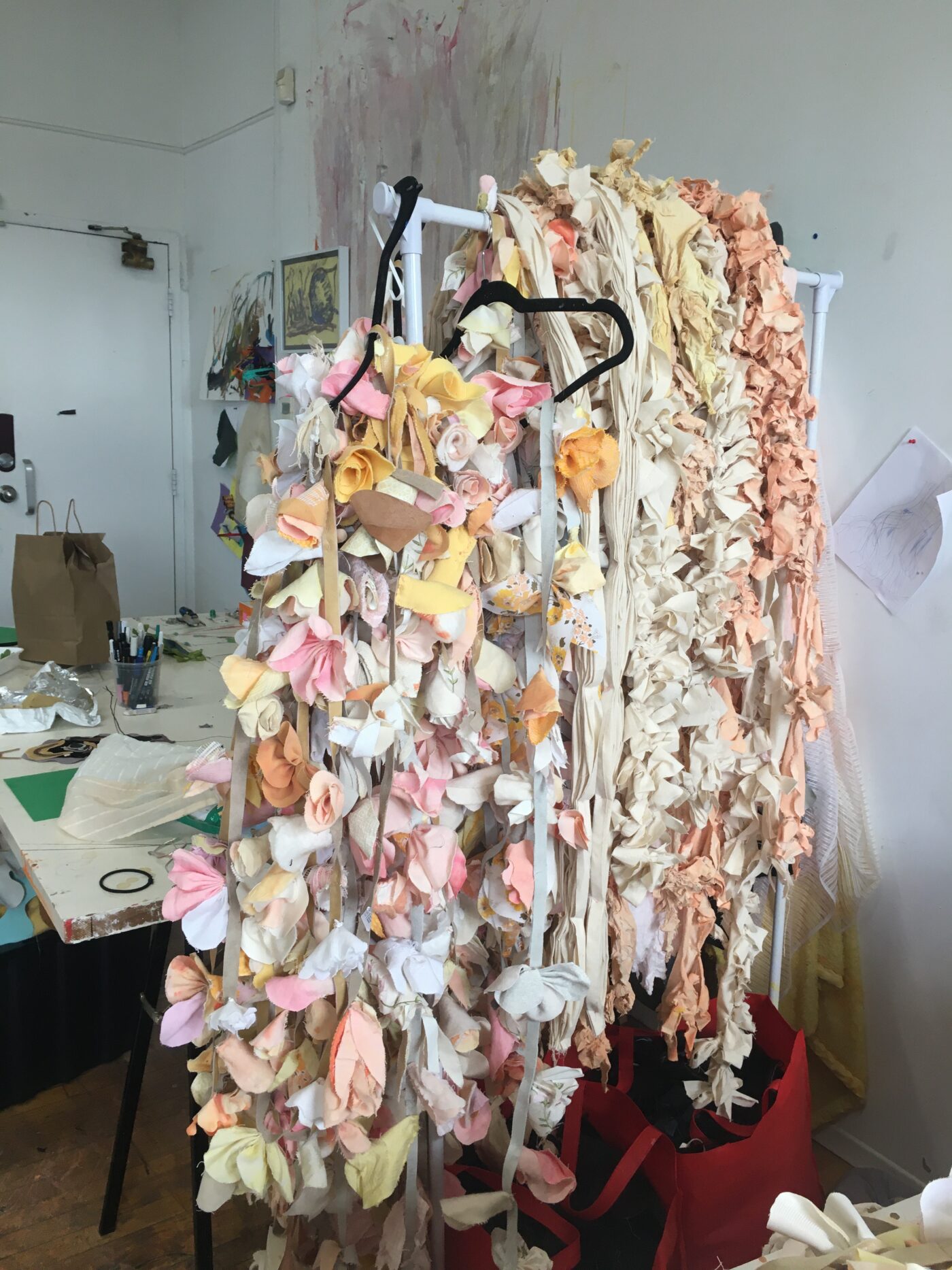 A large pile of textile sculpted flowers. The flowers are various pastel warm tones, ranging from whites, to pink, yellow and orange.